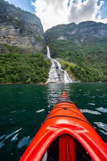 Kayak trip on the Geirangerfjord at the Freier waterfall, tip of a red kayak in the fjord,