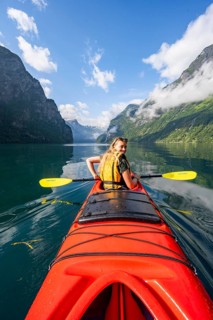 Kayak trip on the Geirangerfjord, young woman paddling in a red kayak, atmospheric fjord landscape,