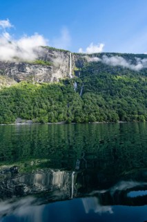 Atmospheric fjord landscape with Gjerdefossen waterfall, on the Geirangerfjord with reflection,