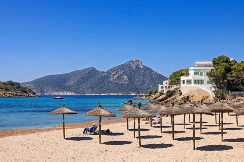 People sunbathing on a sandy beach with parasols by the Mediterranean Sea with white houses on a