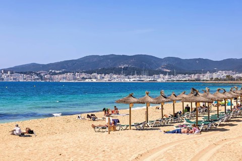 Sand beach by the blue mediterranean sea with sunbathing people at sun lounger and the palma city