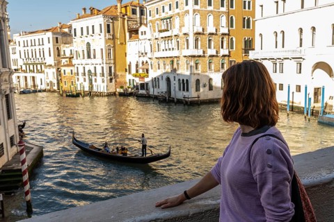 Young woman enjoying picturesque view of traditional gondola sailing on grand canal amidst historic
