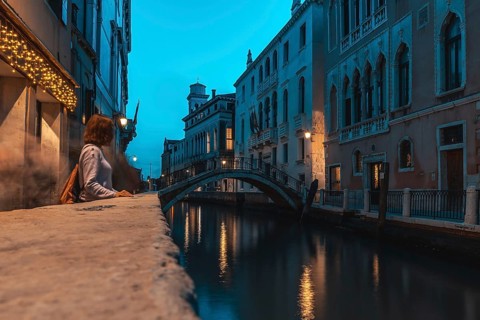 Young woman contemplating venice's canal at blue hour, with a small bridge and typical venetian