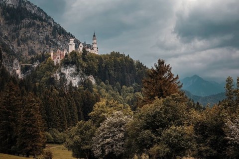 Neuschwanstein Castle towers over a wooded landscape under a dramatic sky, Schwangau, Bavaria