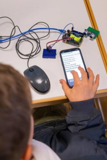 Child operating smartphone next to electronic devices on a table, Youth Research Centre Nagold,