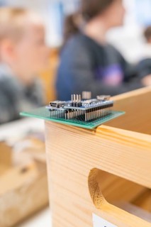 Technological circuit board on a wooden box with blurred people in the background, Nagold Youth