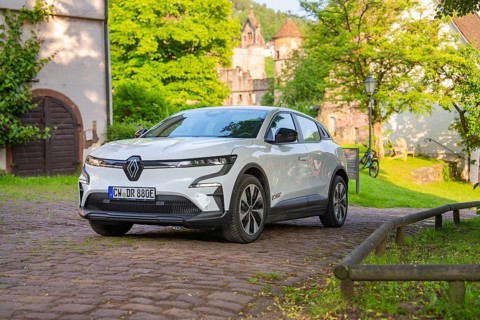 White car parked on a cobbled path in front of old buildings and a green summer backdrop, Renault