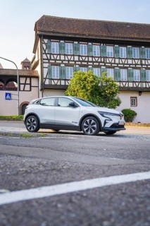 White car parked on an urban street in front of a large, traditional half-timbered house in summer,