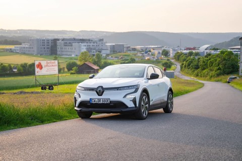 White car parked on a country road with hills and city view in the background, Renault Megane, Deer