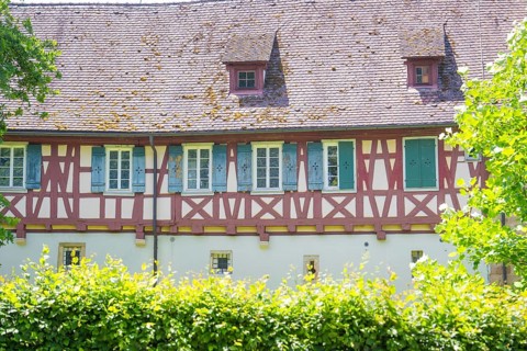 Historic half-timbered house with small windows behind green hedges, event and wedding location
