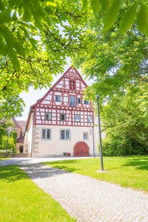 Half-timbered house with cobblestone path and surrounded by green trees under a clear sky, event