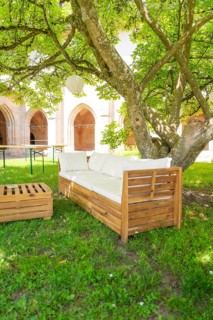 Wooden sofa under a tree in the garden with cushions, located in a shady forecourt, event and