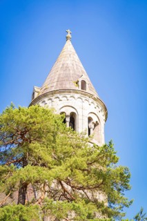 Top of a medieval church tower with a tree in the foreground under a blue sky, event and wedding