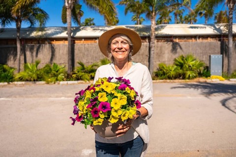 Happy gardener holding a pot of colorful petunias, enjoying a sunny day at the botanical garden