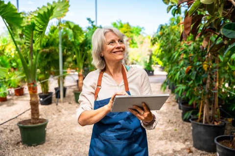 Smiling gardener working in a greenhouse, using a digital tablet while surrounded by vibrant plants