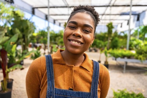 Portrait of a young african american woman working in a greenhouse, smiling confidently amidst lush