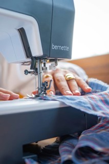 Focus on a sewing machine processing fabric, hand-guided and adorned with a gold ring