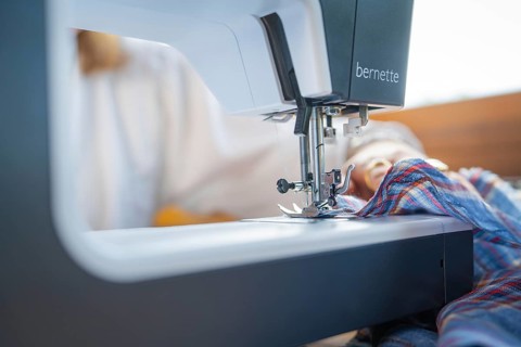 Details of the sewing process with needle and fabric in a well-lit environment, focus on the