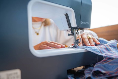 Sewing a chequered fabric with a sewing machine, hands guide the fabric under the needle