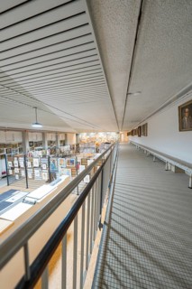 A corridor on the upper floor with a view of a large art gallery decorated with various works,