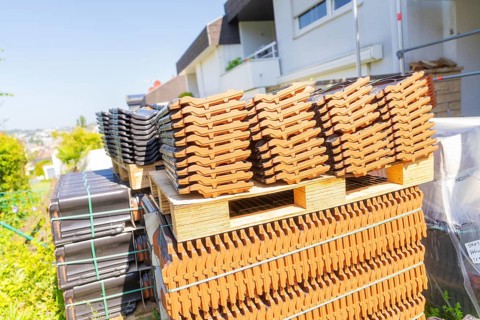 Stacked roof tiles on pallets outdoors in sunny weather, roof renovation, house construction,