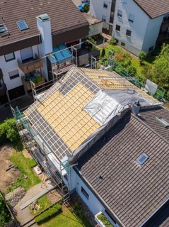 House with scaffolding and part of the roof covered, in a sunny residential area, roof renovation,