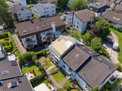 Aerial view of a residential area with a house showing roof work in the middle of green areas, roof