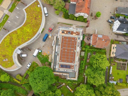 Bird's eye view of building with roof, surrounded by trees and construction site activities,