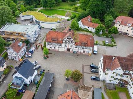 Historic half-timbered houses with red tiled roofs surrounded by cobblestones and green spaces,