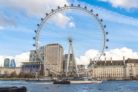 The london eye majestically stands tall on the banks of the river thames, with a boat sailing by