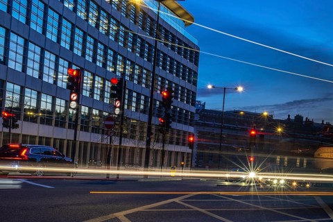 Cars passing by on a london street at dusk, with traffic lights turning red and offices in the