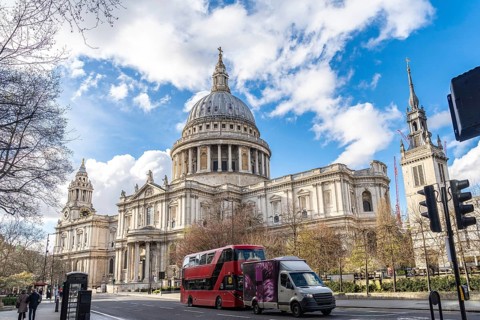 Red double decker bus driving on a street next to st paul's cathedral in london, uk, on a sunny