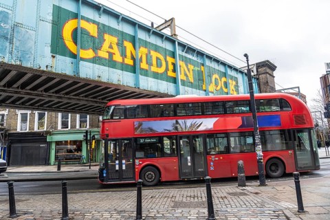 Iconic red double decker bus driving through camden town in london, under the bridge with the