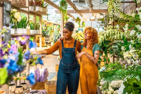 Two young women working together in a garden center, discussing vibrant plants and creative flower