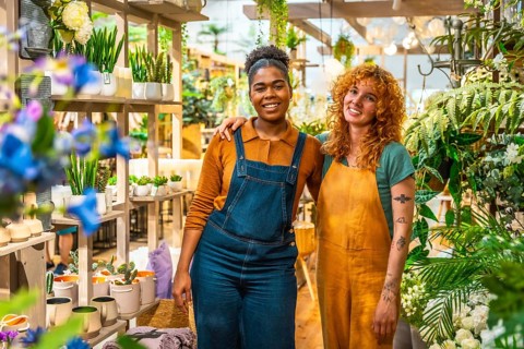Two joyful florists posing together in their vibrant flower shop, surrounded by a colorful array of
