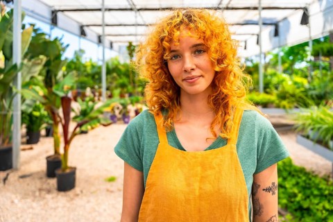 Confident young female gardener working in a vibrant greenhouse, surrounded by thriving plants and