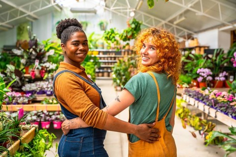 Two happy florists are hugging each other, smiling, while working in their plant nursery greenhouse