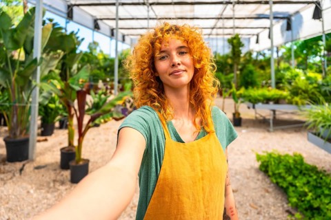 Confident red haired female gardener taking a selfie in a greenhouse, showcasing her passion for