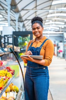 Young supermarket employee managing fresh fruit section inventory using a digital tablet, ensuring