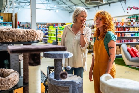 Happy senior woman selecting a cat tree while receiving assistance from a friendly shop assistant