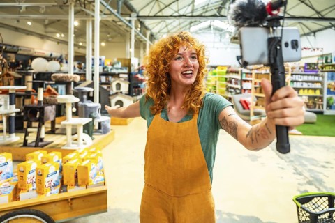 Young saleswoman filming a video for social media with a smartphone and microphone, showing pet