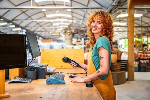 Young saleswoman holding barcode scanner, ready to scan products at checkout counter in modern