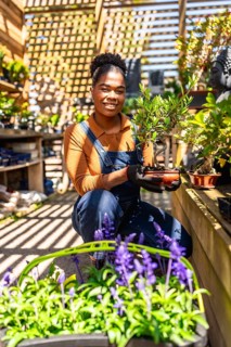 Young woman working in a vibrant greenhouse, holding a small bonsai tree, surrounded by flourishing