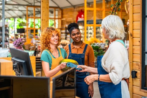 Customer paying with contactless payment in a grocery store, assisted by two smiling shop