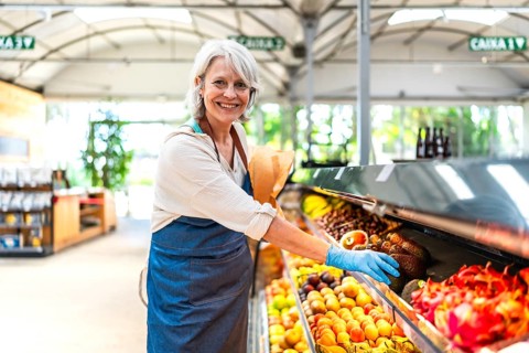 Smiling greengrocer wearing protective gloves, carefully arranging a vibrant display of fresh fruit