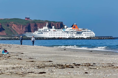 Tourists and photographers on the beach of the Heligoland dune, cruise ship in front of cliffs,