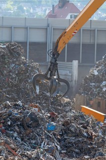 Hydraulic crane lifts scrap metal at the scrap yard in the background City of Plochingen
