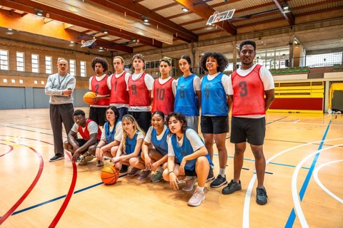 High school basketball team posing for a photo with their coach on the court, ready for the game,