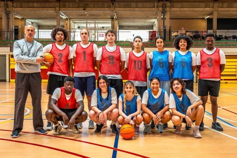 Diverse high school basketball team posing confidently for a group photo with their coach on the