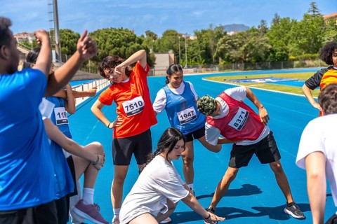 Teenagers wearing bib numbers stretching together on a blue running track before a track and field